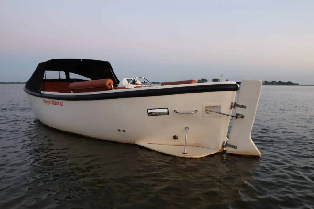 Witte open sloep op rustig water bij zonsondergang